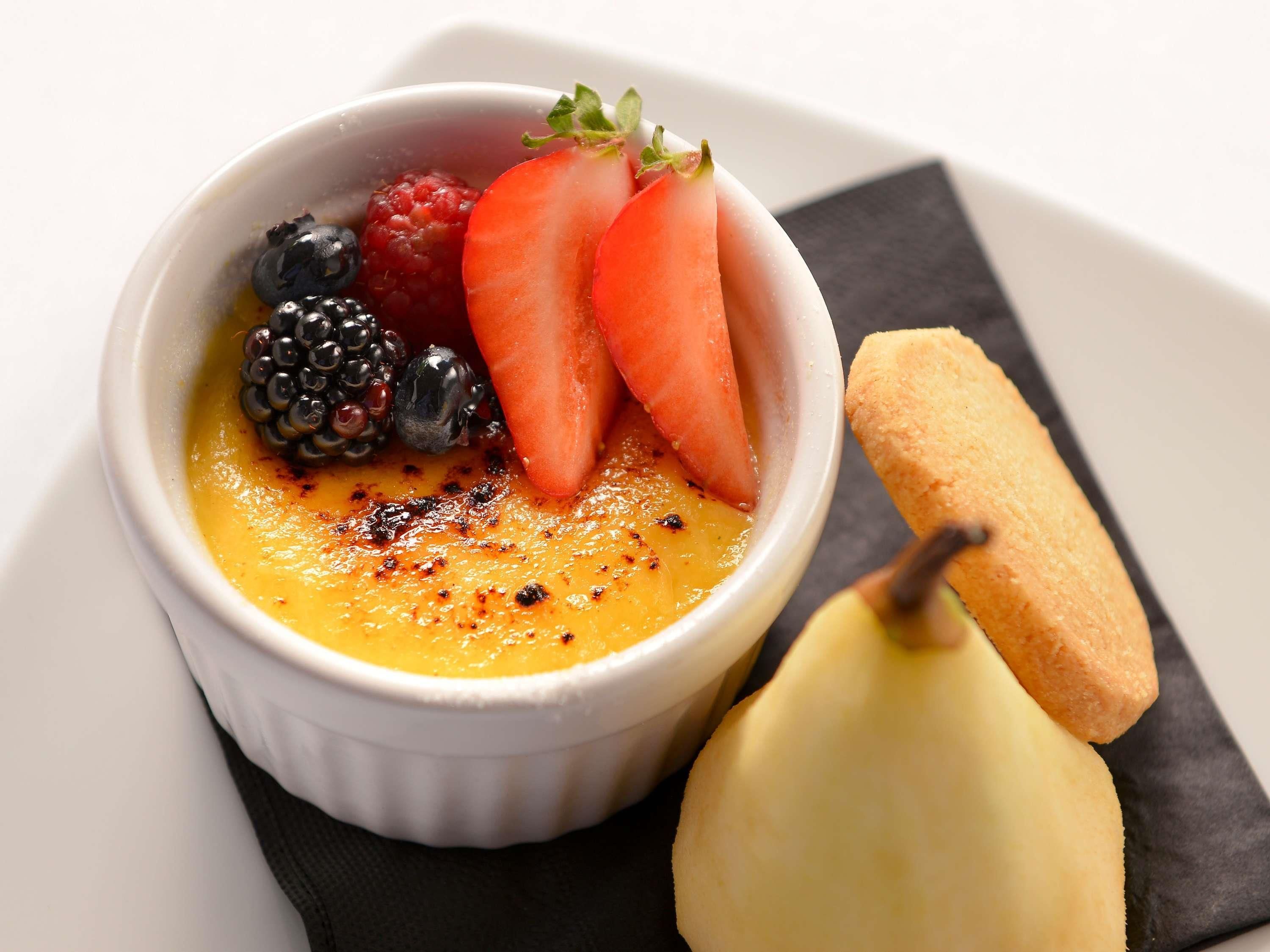 Postre en una ramequín blanca con fresas, zarzamoras y una pera sobre una servilleta negra.