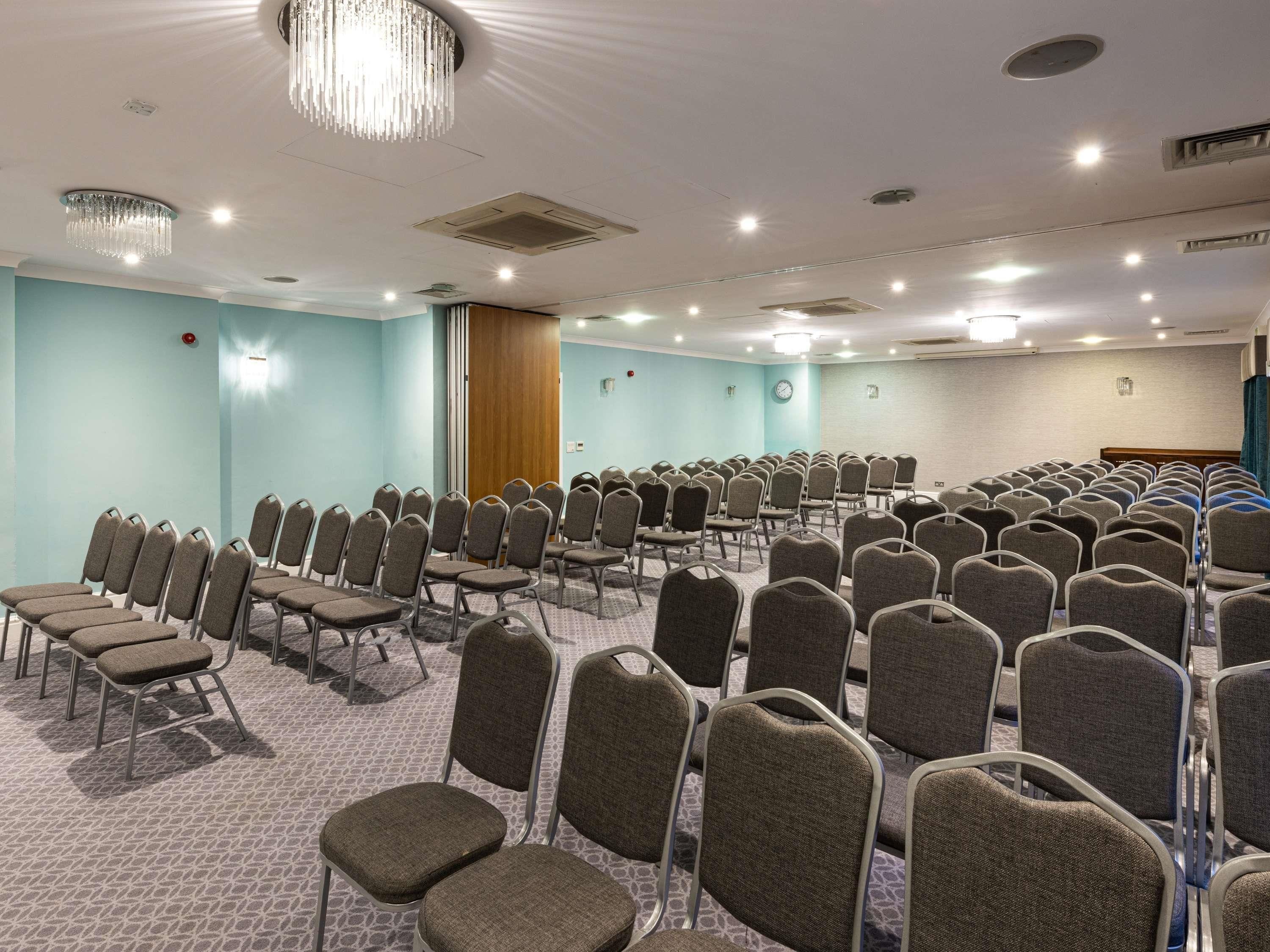 A conference room with rows of chairs, a clock, and a wooden door.
