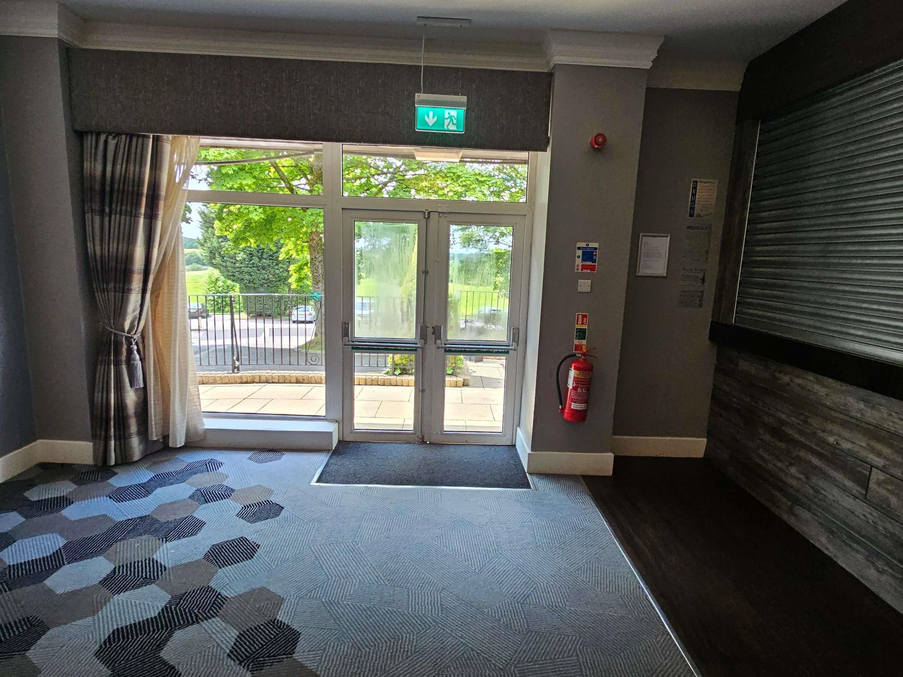 L’entrée d’un hôtel, avec un tapis à motifs, un extincteur et une porte de volet fermée.