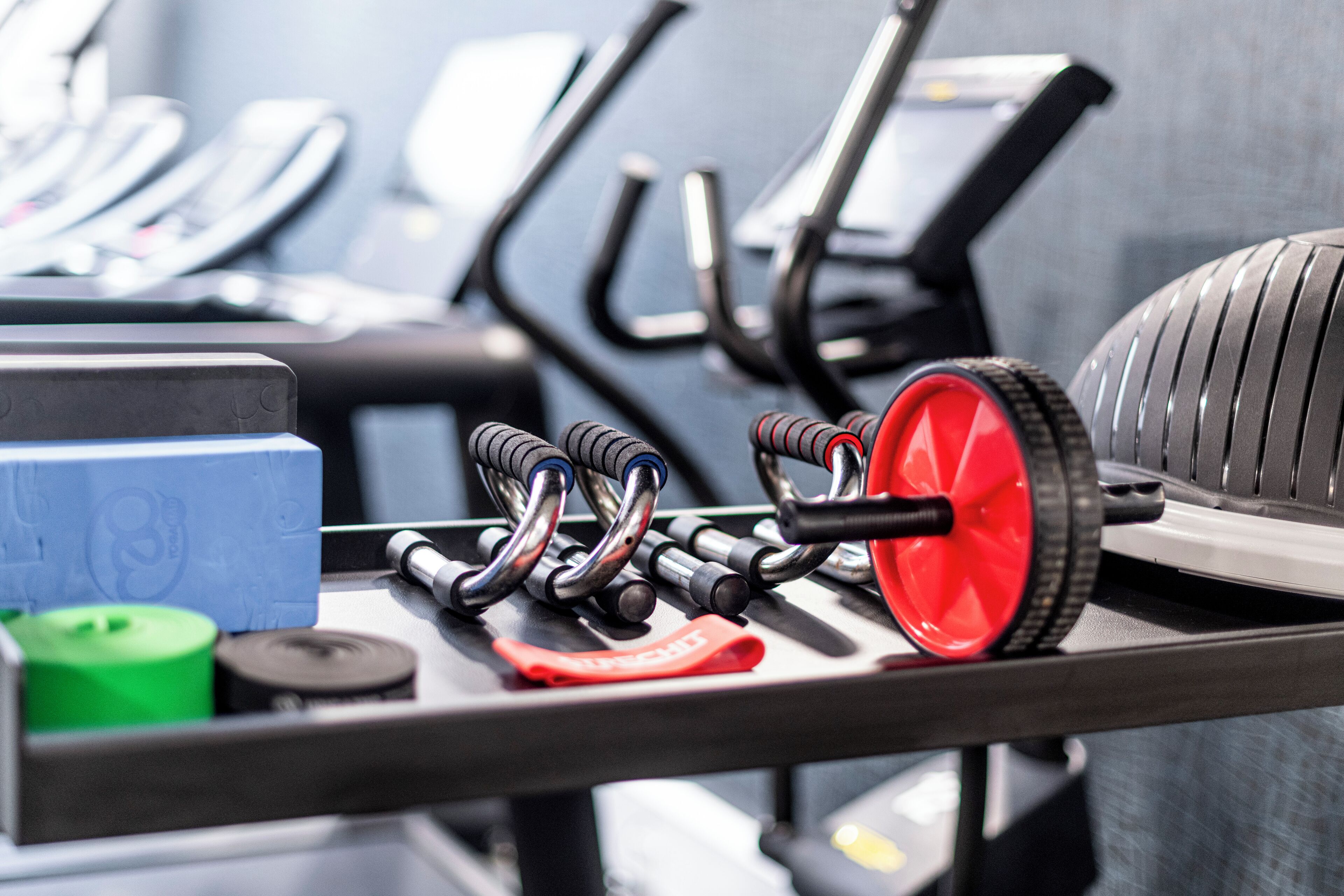 Fitnessgeräte, darunter Gewichte, ein rotes Rad und Trainingsmaschinen.