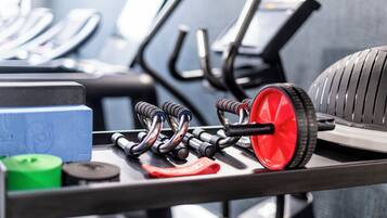 Fitnessgeräte, darunter Gewichte, ein rotes Rad und Trainingsmaschinen.