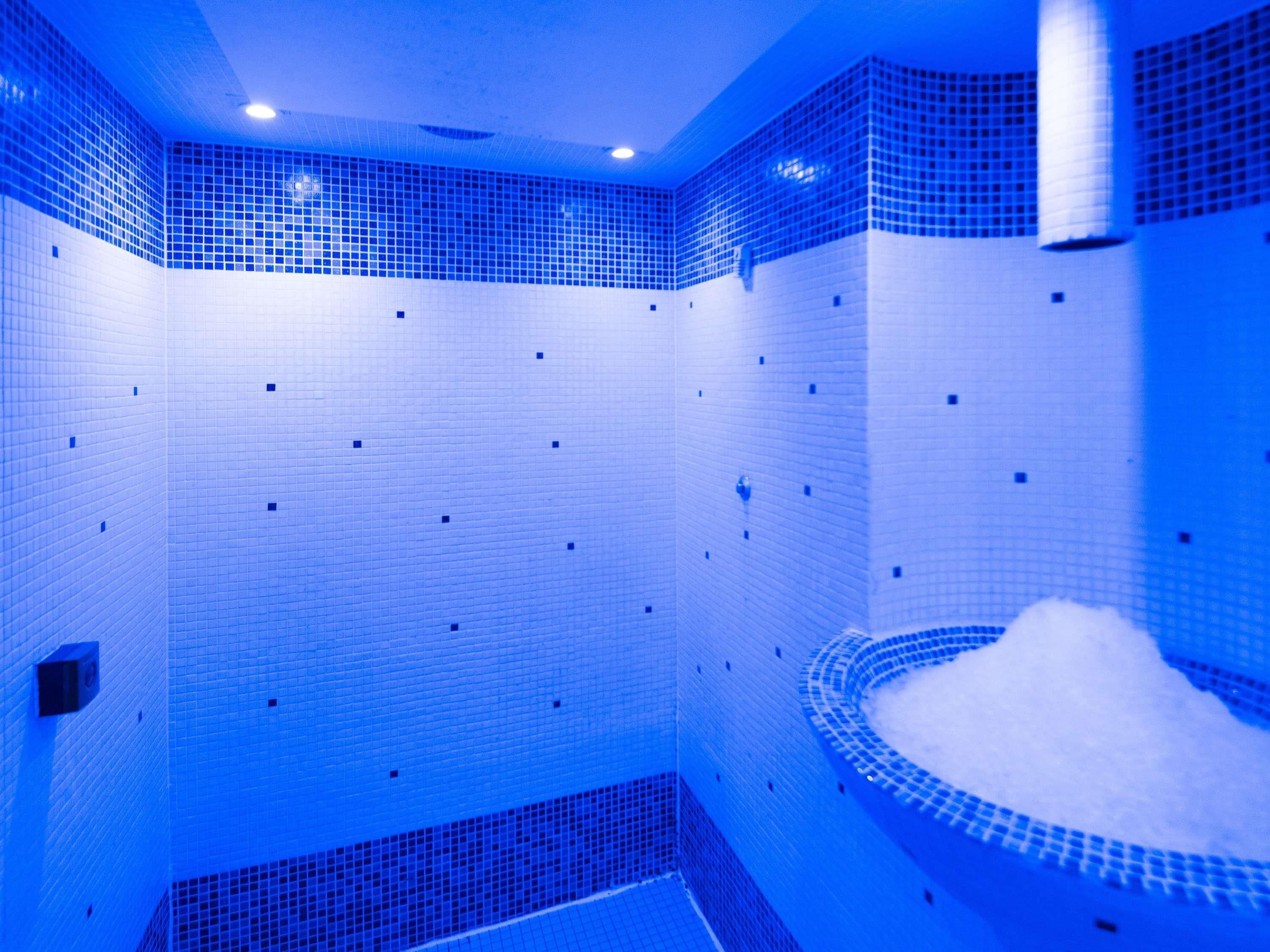 Een kamer met blauwe tegels, een rond ligbad en een klein wastafeltje.