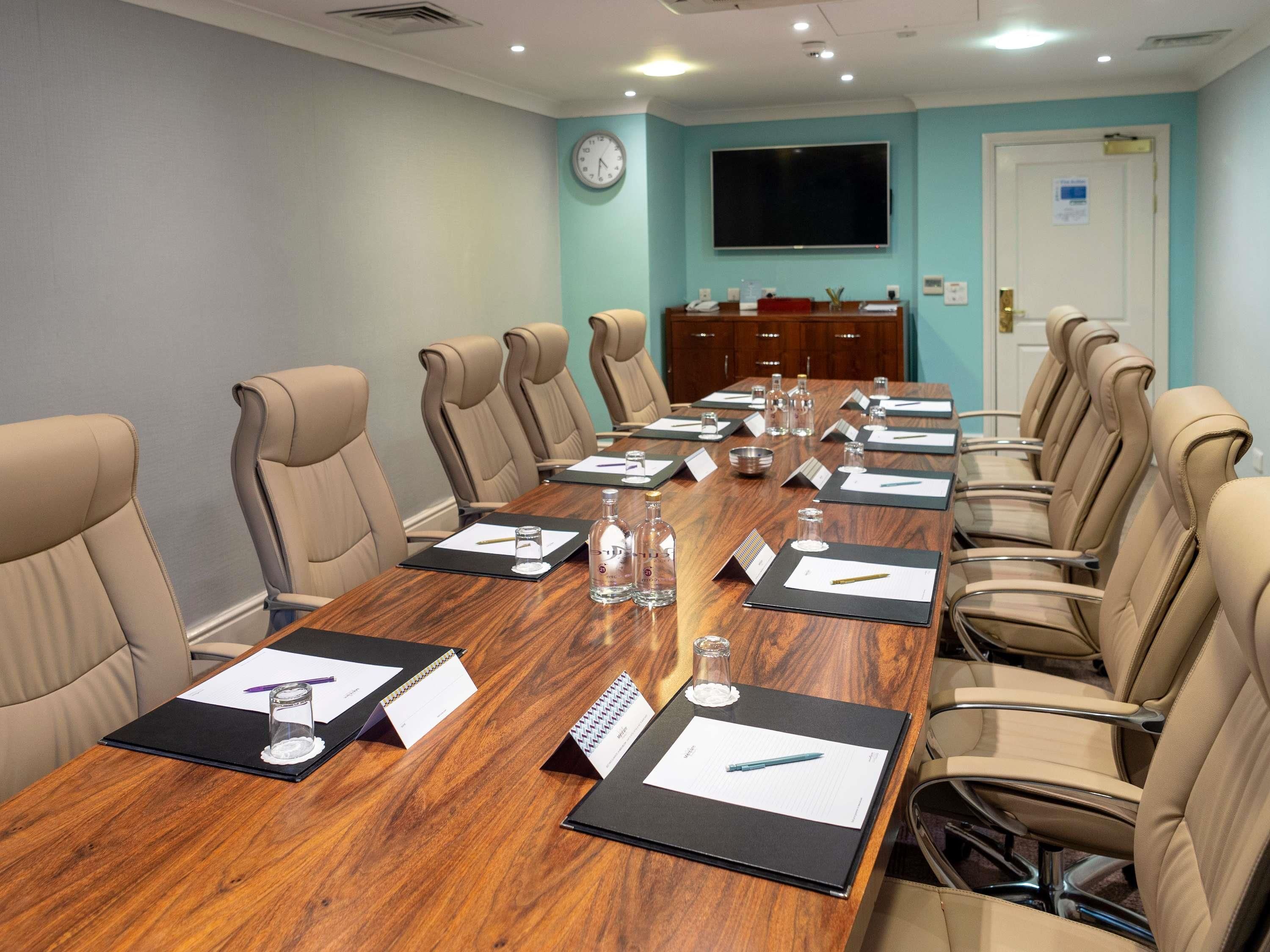 A conference room with a long table, beige chairs, nameplates, and a clock on the wall.