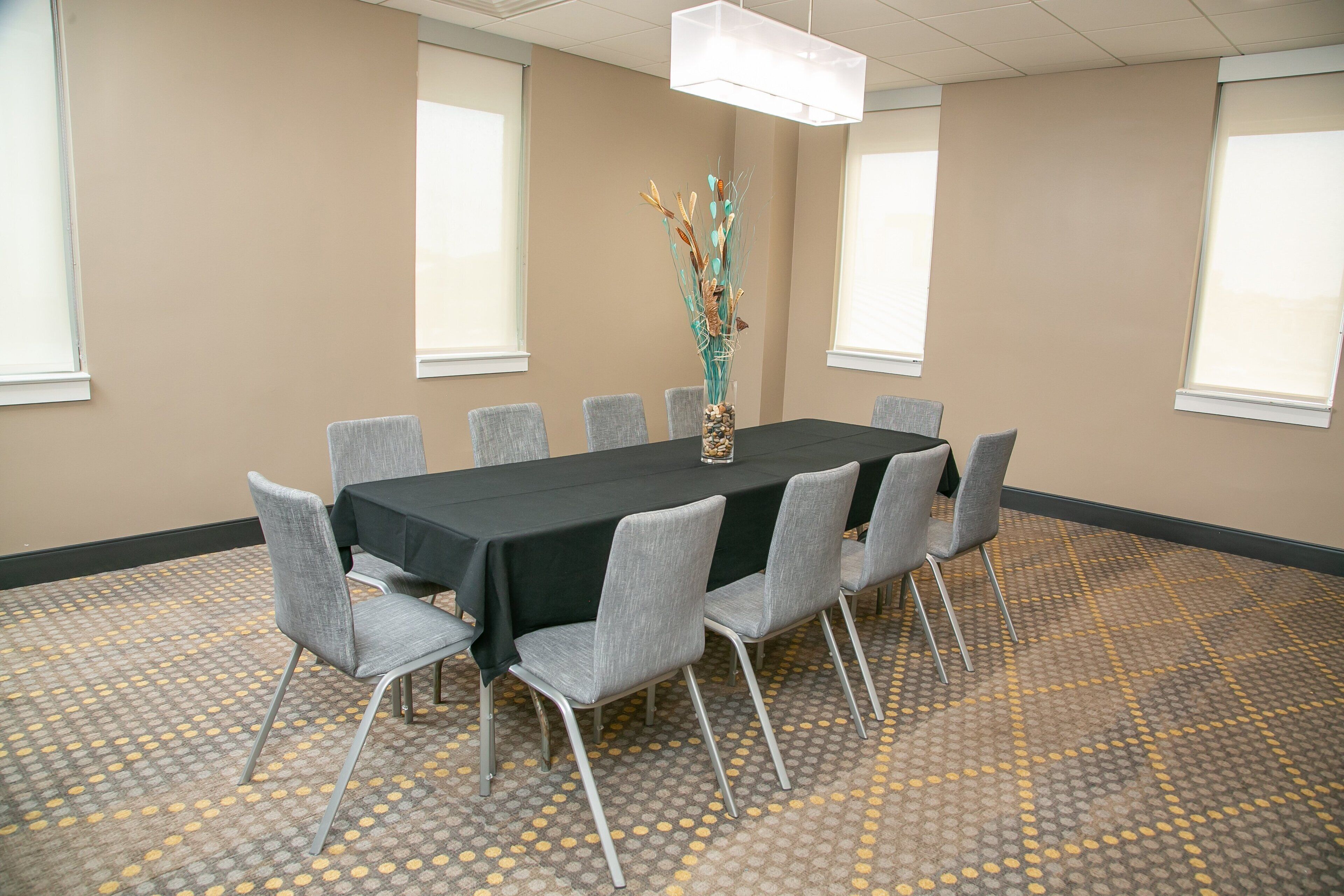 A conference room with a rectangular table, grey chairs, a decorative vase, and patterned carpet.