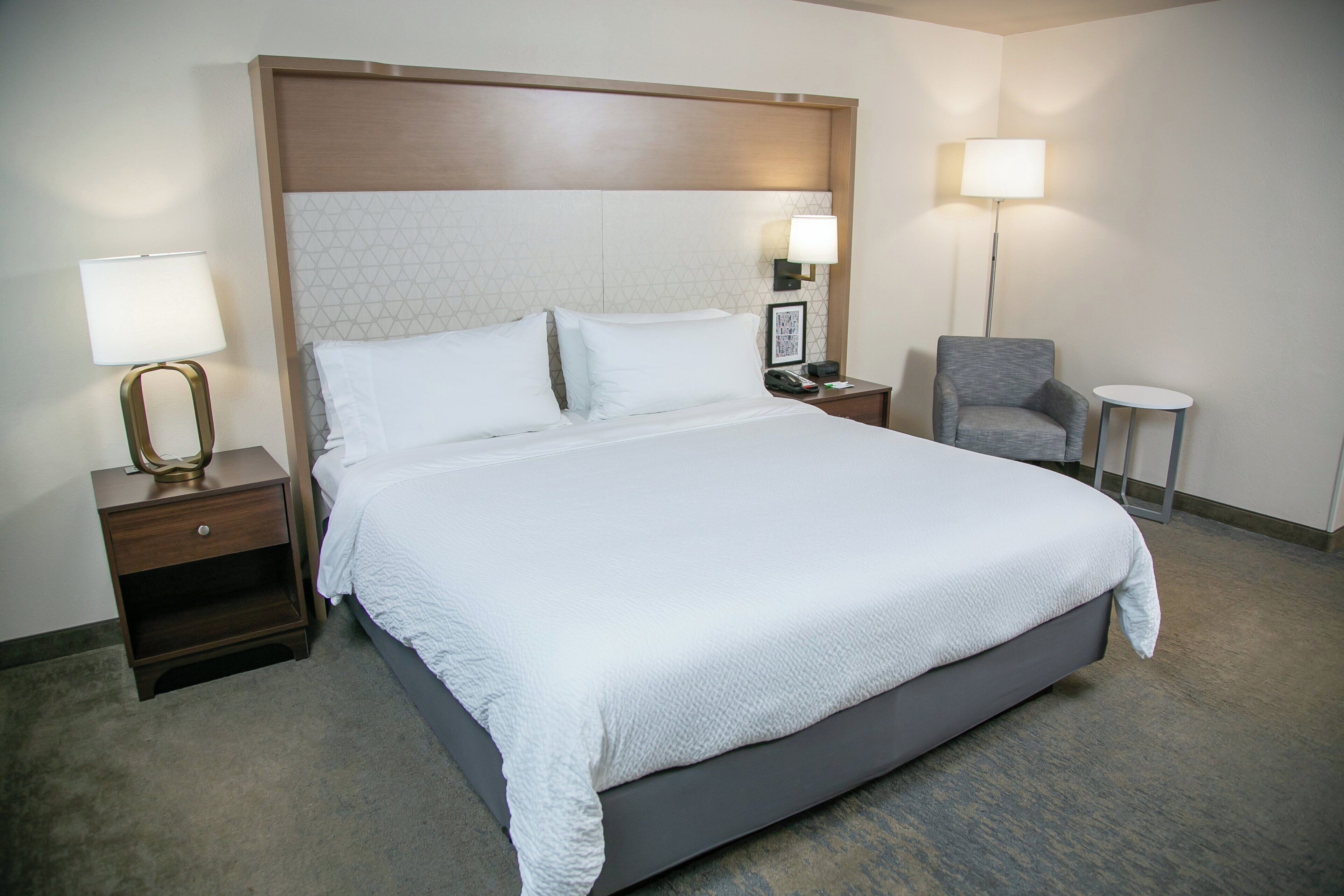 A hotel room with a large bed, a nightstand with a lamp, a chair, and a small table.