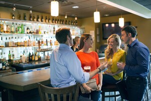 Un área de bar con una variedad de botellas en estantes, sillas de madera y luces colgantes.