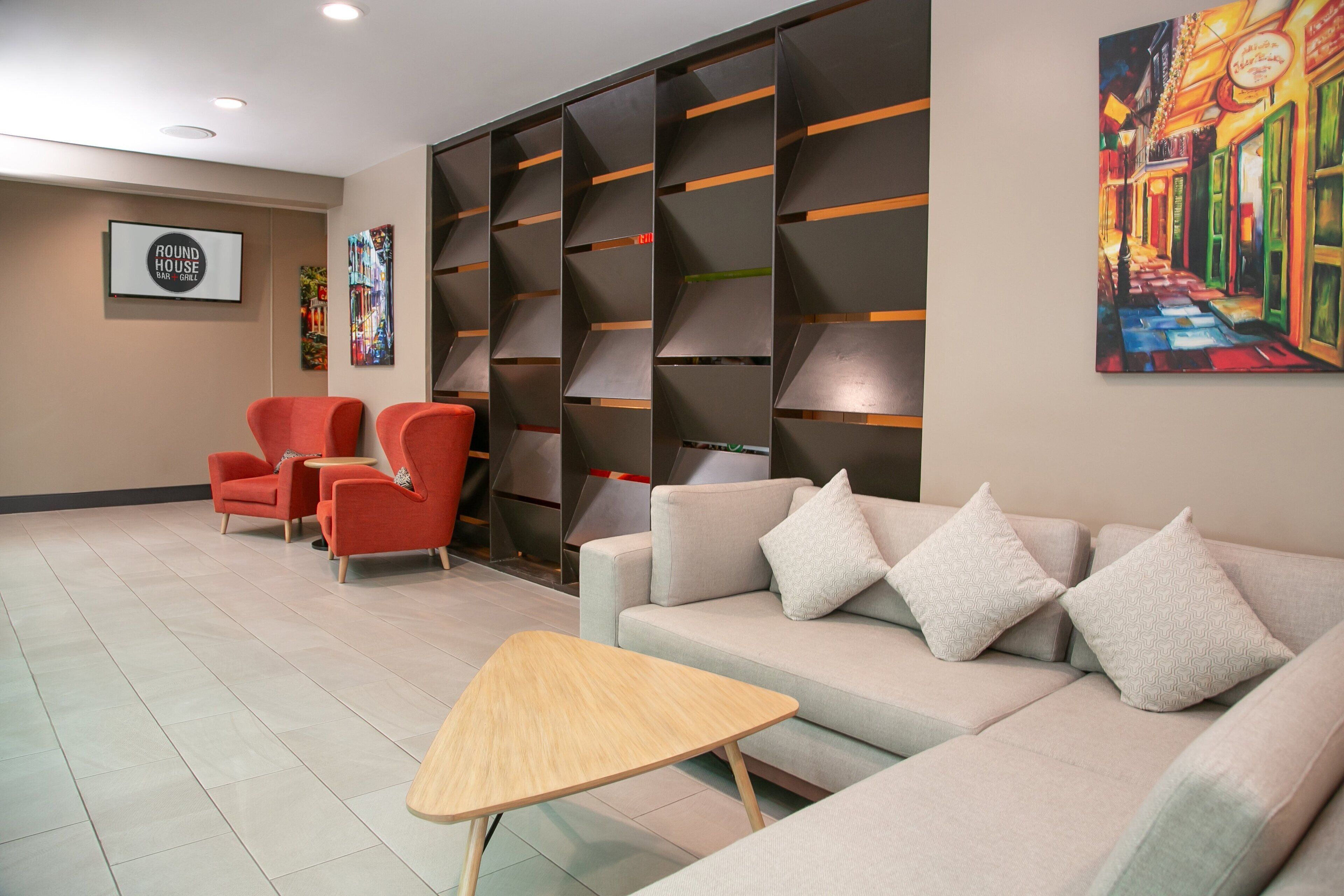 Un hall d’entrée moderne avec un canapé, des fauteuils rouges, une table en bois et une bibliothèque.