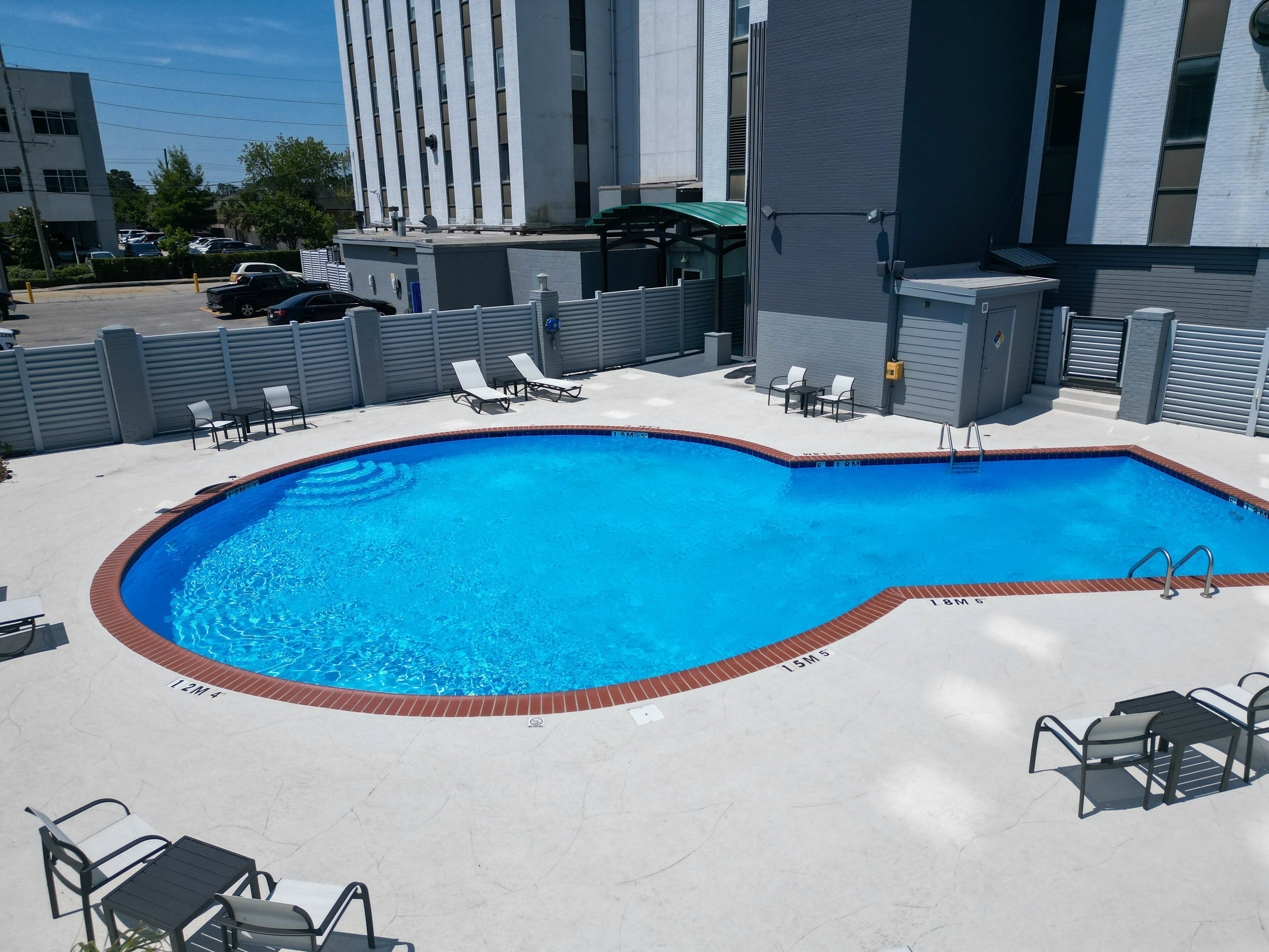 A rectangular swimming pool with a brick edge, surrounded by lounge chairs and a table.