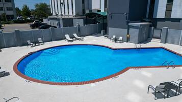 A rectangular swimming pool with a brick edge, surrounded by lounge chairs and a table.