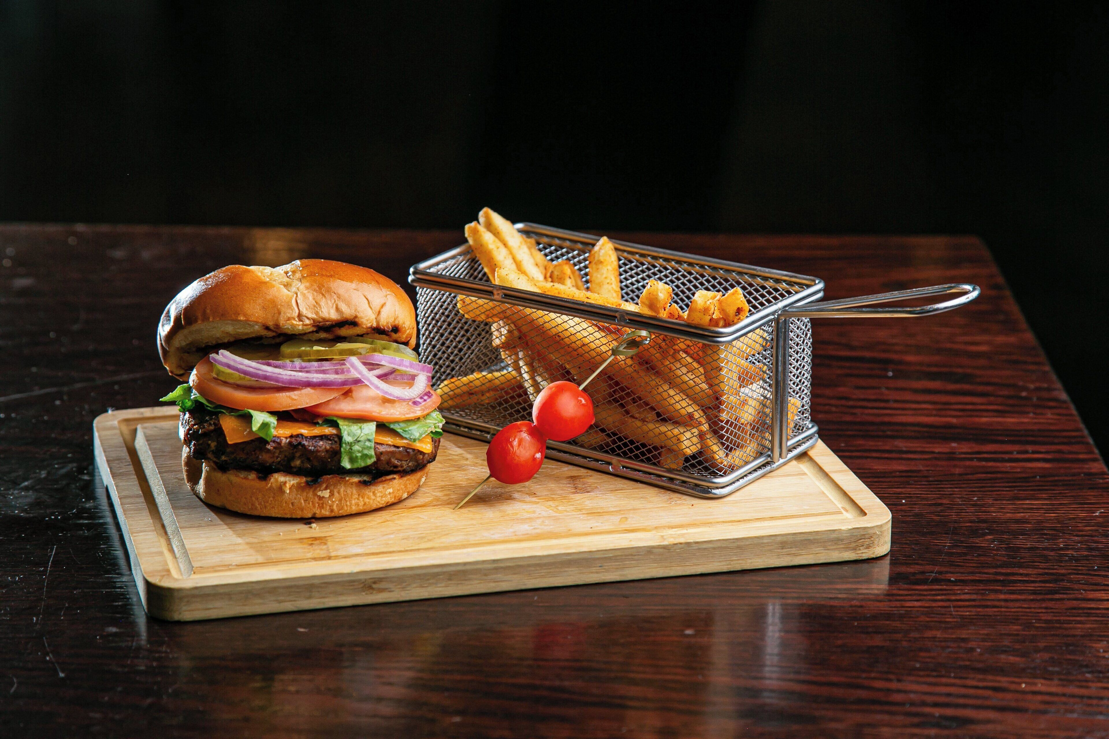 A burger with fries on a wooden board.