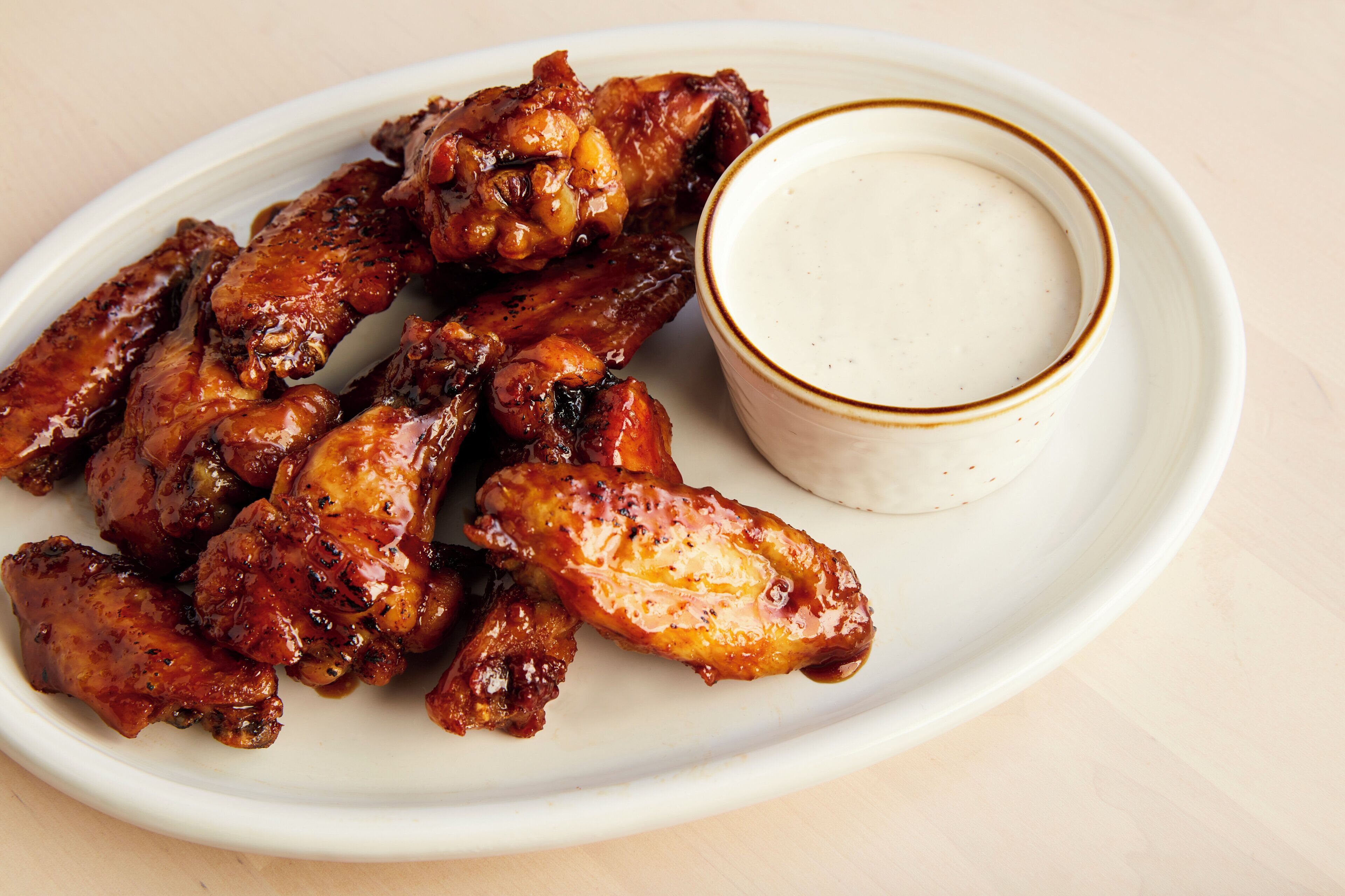 A plate of glazed chicken wings with a side of dipping sauce.