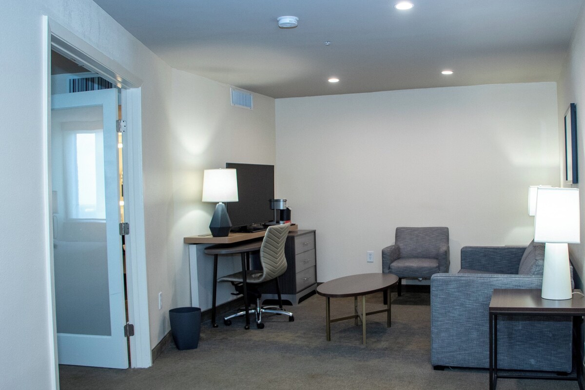 Una habitación de hotel con escritorio, silla de oficina, sofá y una mesita de noche con lámpara.