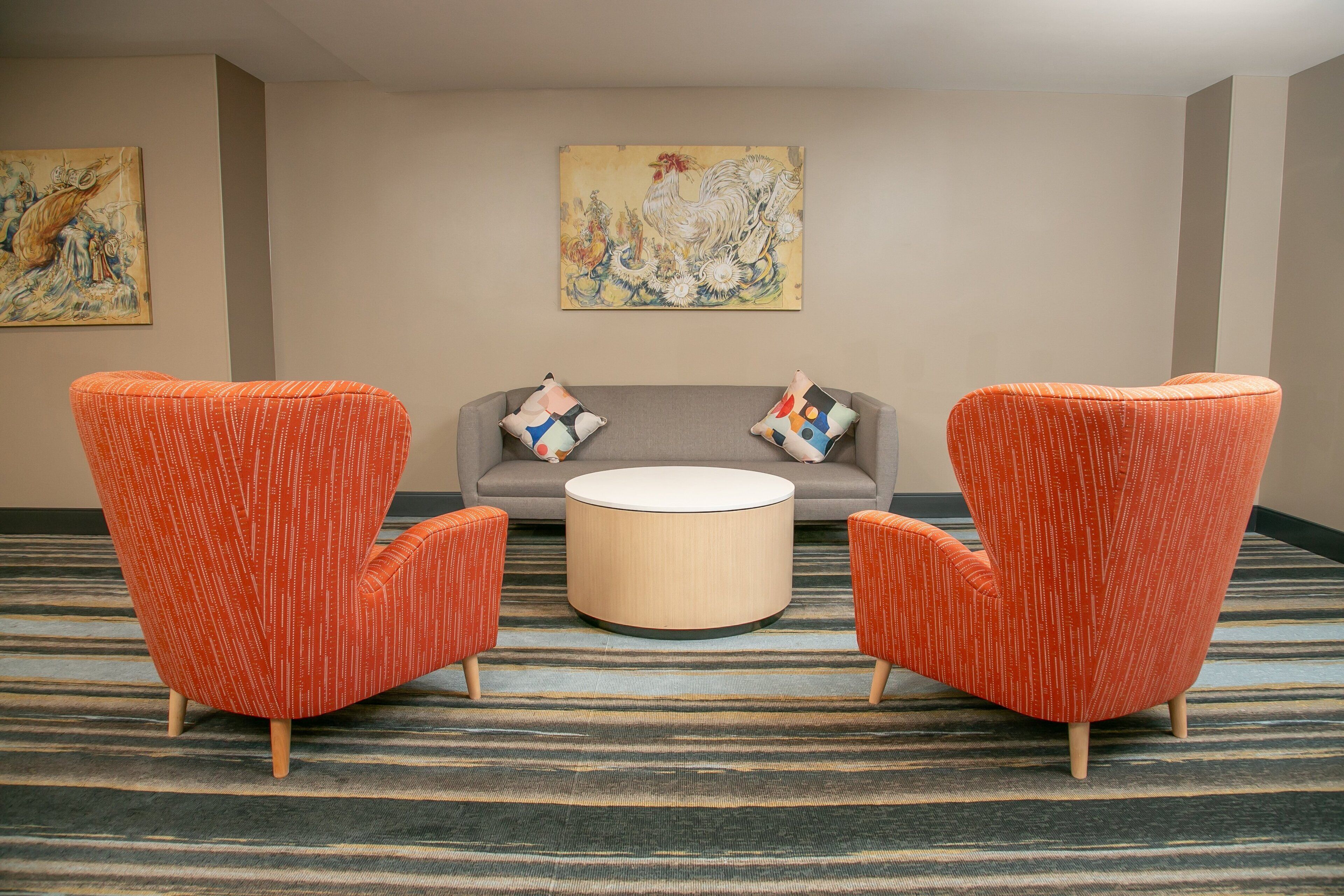 A room with two orange armchairs, a grey sofa, and a round coffee table. There are two paintings on the walls.