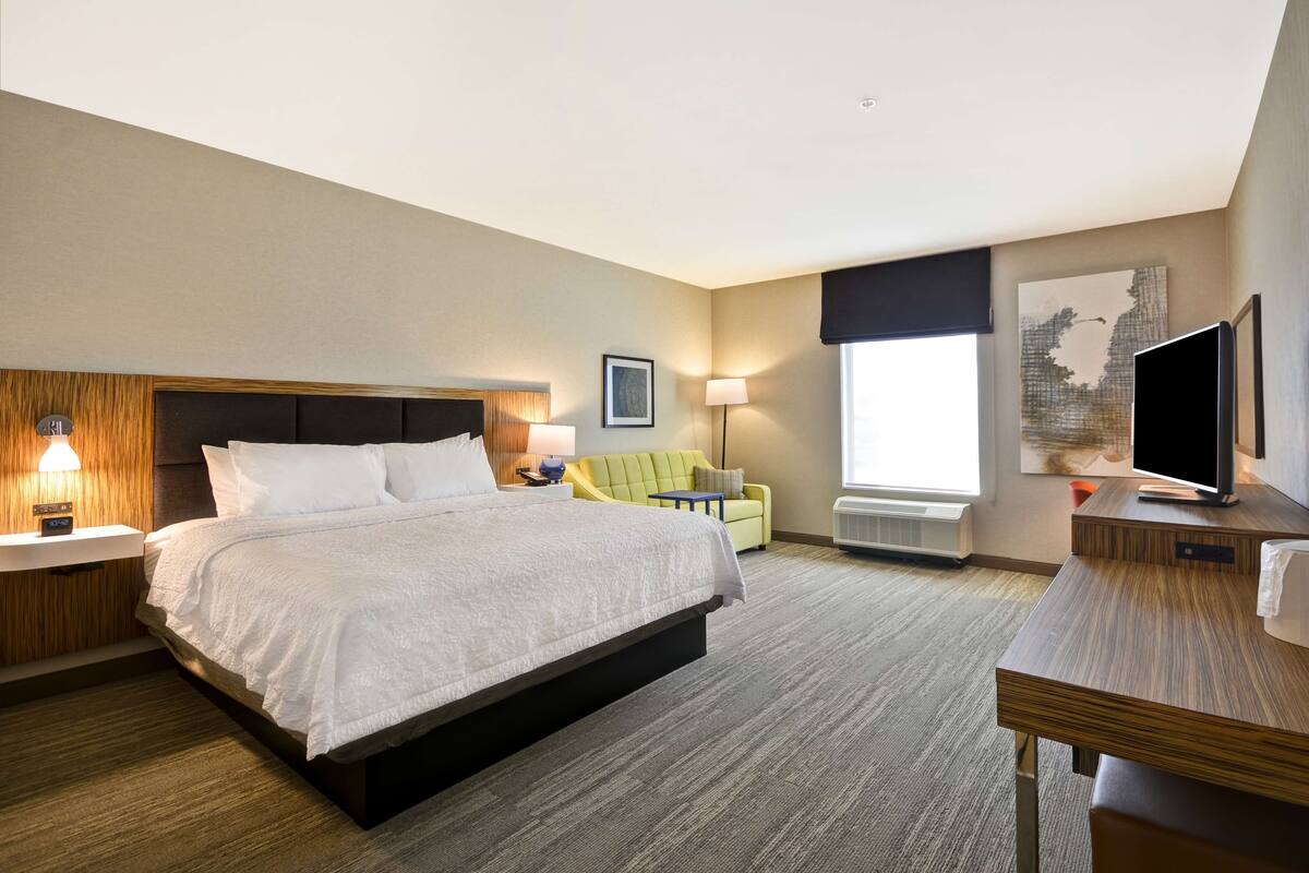 A hotel room with a large bed, a desk, a chair, a TV, and a window.