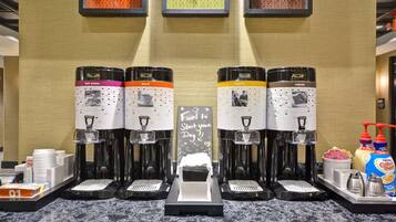 Vier koffieautomaatjes met verschillende labels voor heet water, gewone en sterke koffie, en een bord met de tekst 'Brandstof voor een Goede Start!'