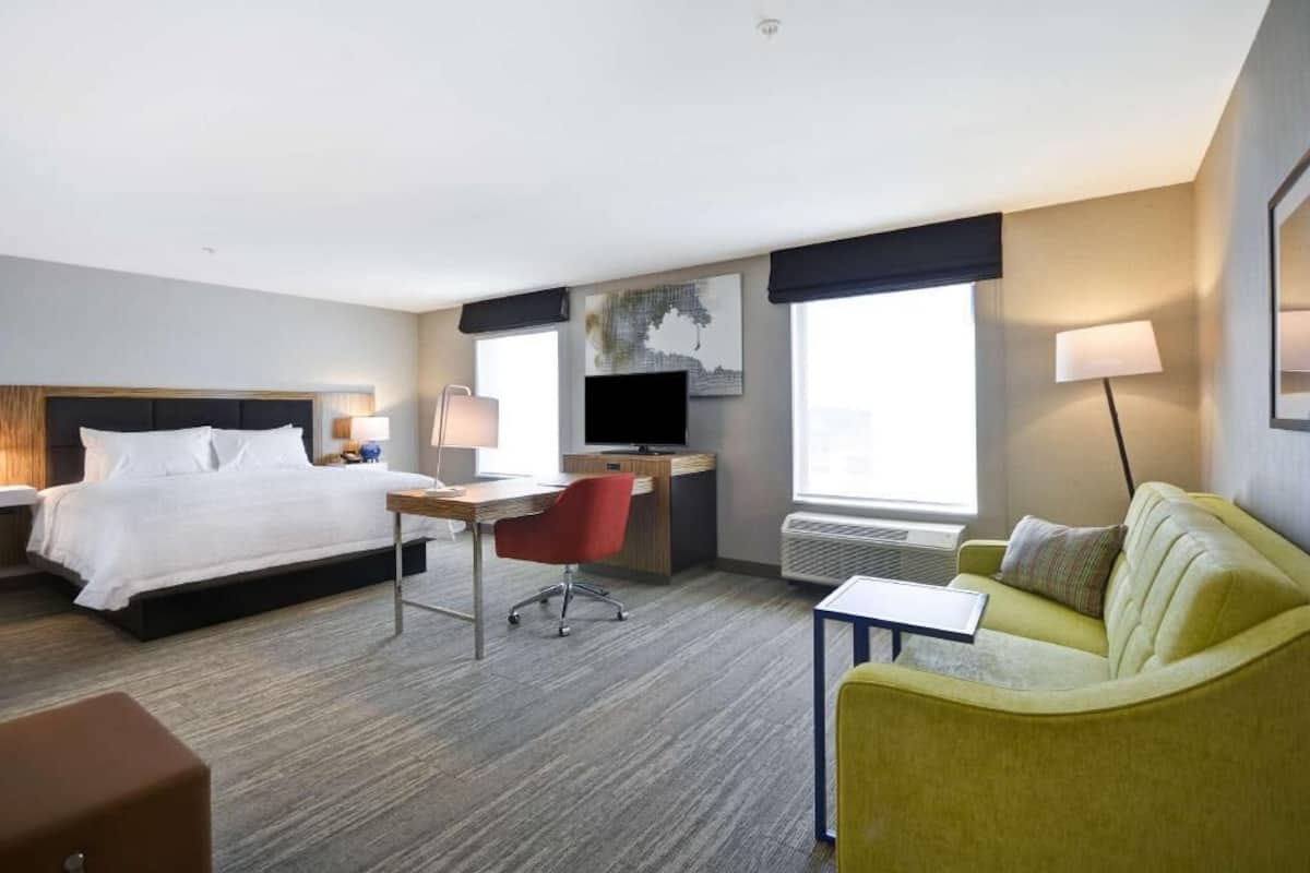 A hotel room with a bed, desk, chair, couch, and a TV.