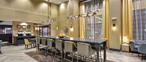 A hotel lobby with a long bar, seating area, and a large window with curtains.