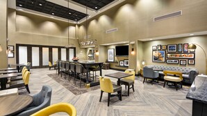 Een ruime hotellobby met een hoge plafond, meerdere zithoeken waaronder een bar, en diverse aan de muur bevestigde kunstwerken.