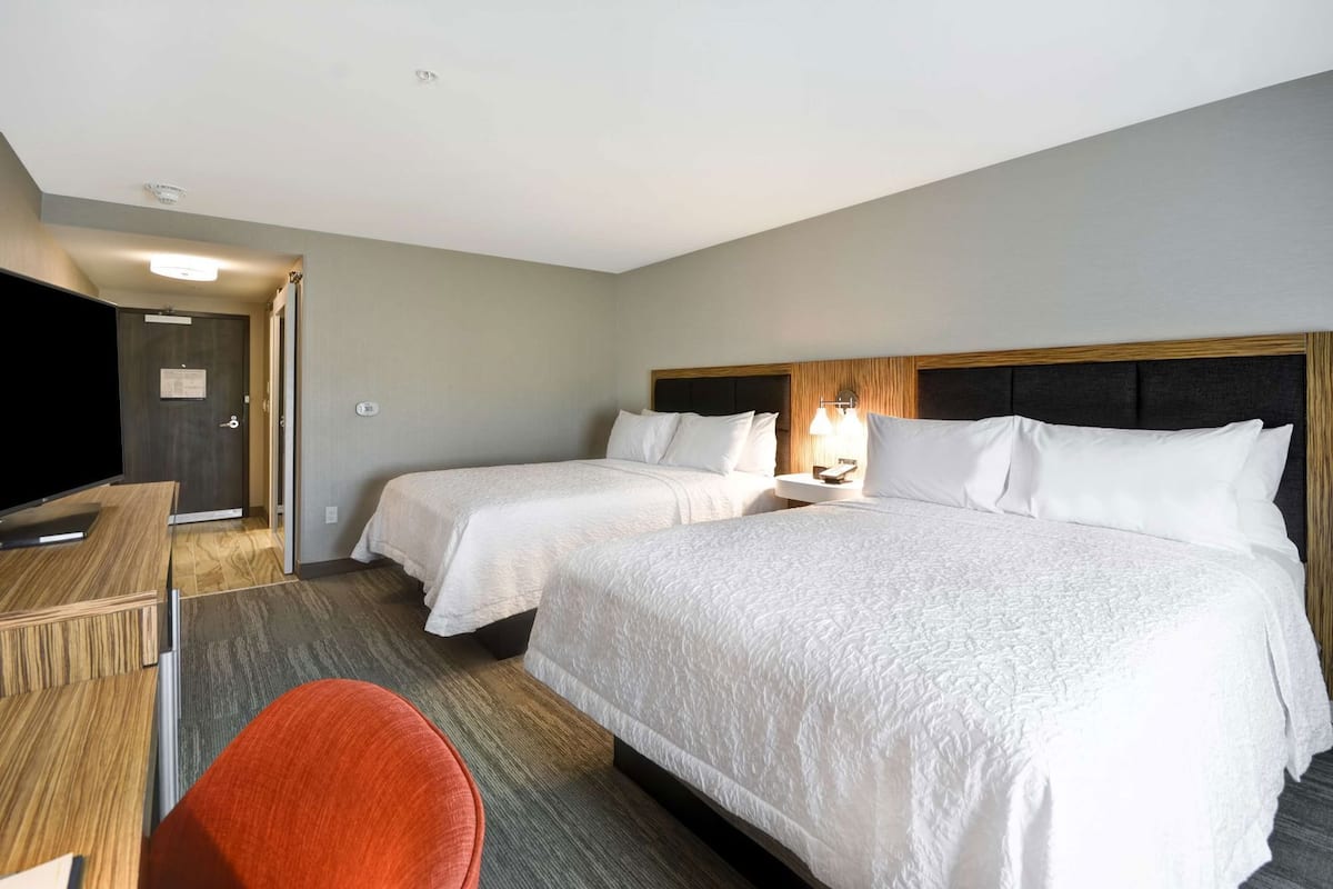A hotel room with two beds, a desk, a TV, and a chair.