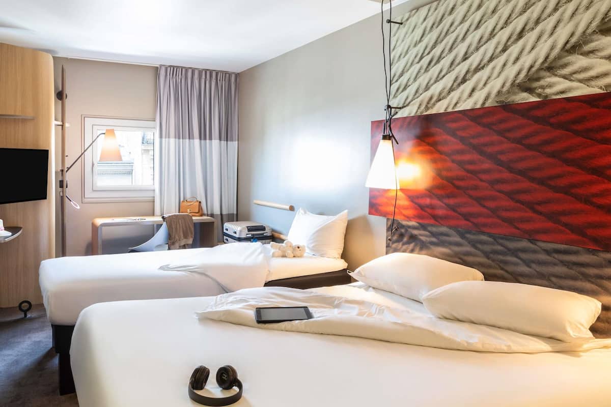 A hotel room with two beds, a desk, a chair, a TV, and a window with curtains.