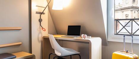 Habitación de hotel pequeña con escritorio, silla, ordenador portátil y maleta.