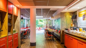 Interior de un restaurante moderno con suelo de madera, mobiliario rojo y negro y una columna central.