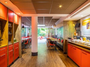 Interior de un restaurante moderno con suelo de madera, mobiliario rojo y negro y una columna central.