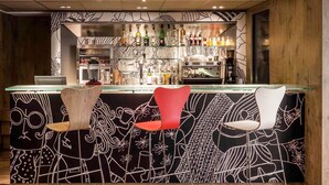 Una zona de bar con mostrador, taburetes y una variedad de botellas y vasos.