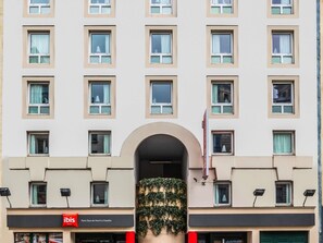 Eine Hotelschaufassade mit zahlreichen Fenstern, einem zentralen Bogen und einer mit Efeu bewachsenen Mauer.