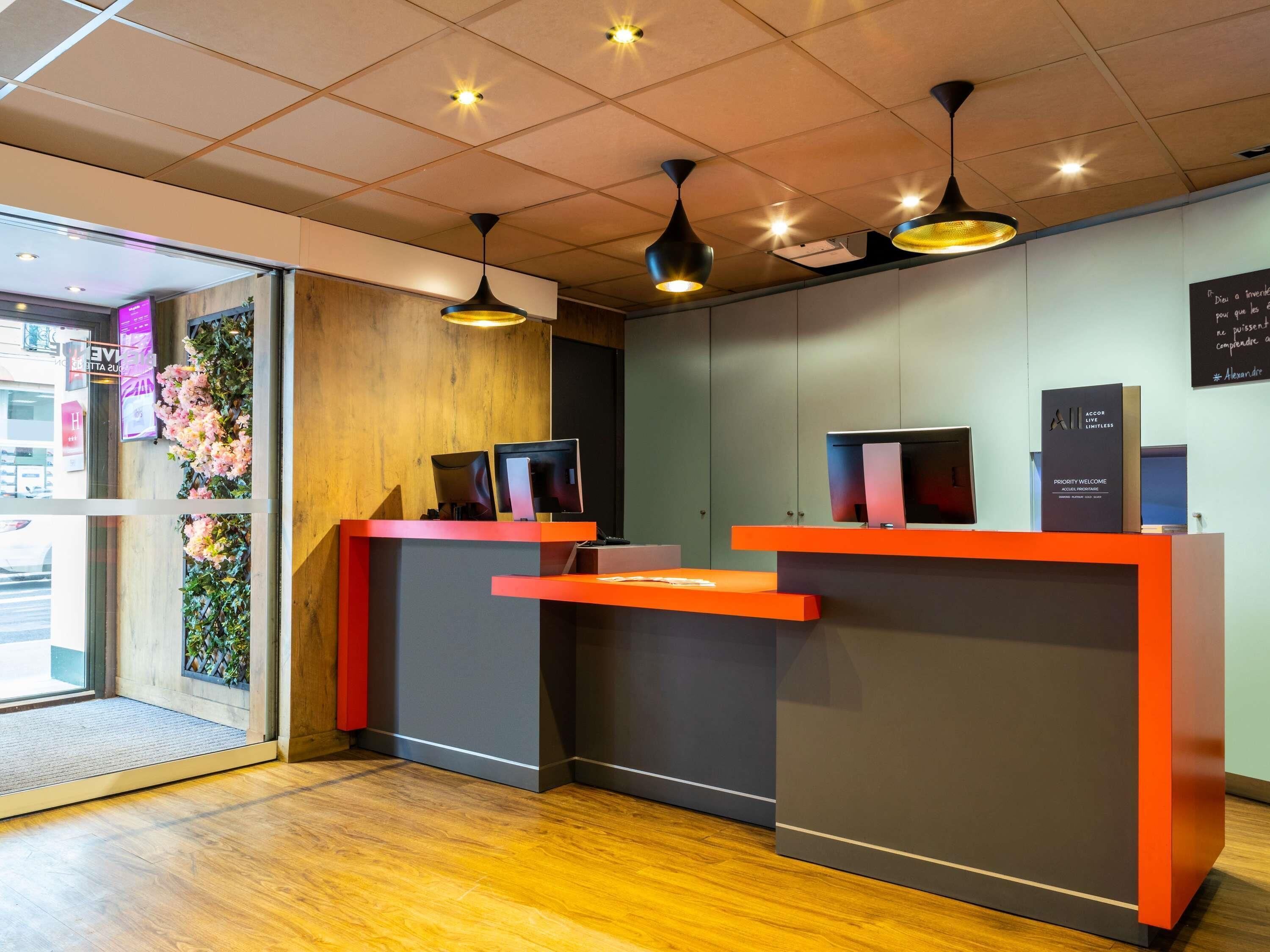 A reception desk with two monitors, a priority welcome sign, and a wooden accent wall.