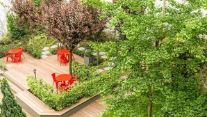 Un patio jardín con mobiliario rojo, senderos de piedra y abundante vegetación.