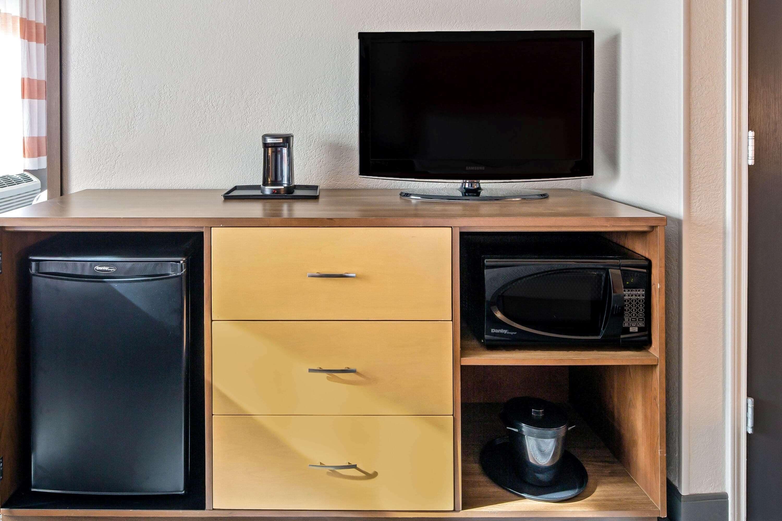 Een compact keukenhoekje met een koelkast, magnetron en een flatscreen televisie op een houten aanrecht.
