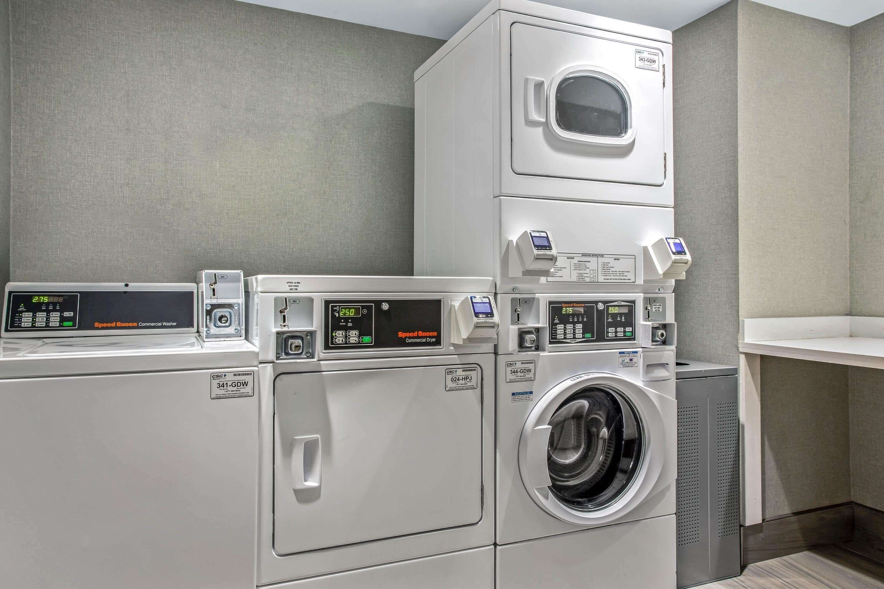 A commercial laundry area with stacked washers and dryers, control panels, and a ventilation unit.