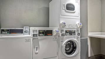 A commercial laundry area with stacked washers and dryers, control panels, and a ventilation unit.
