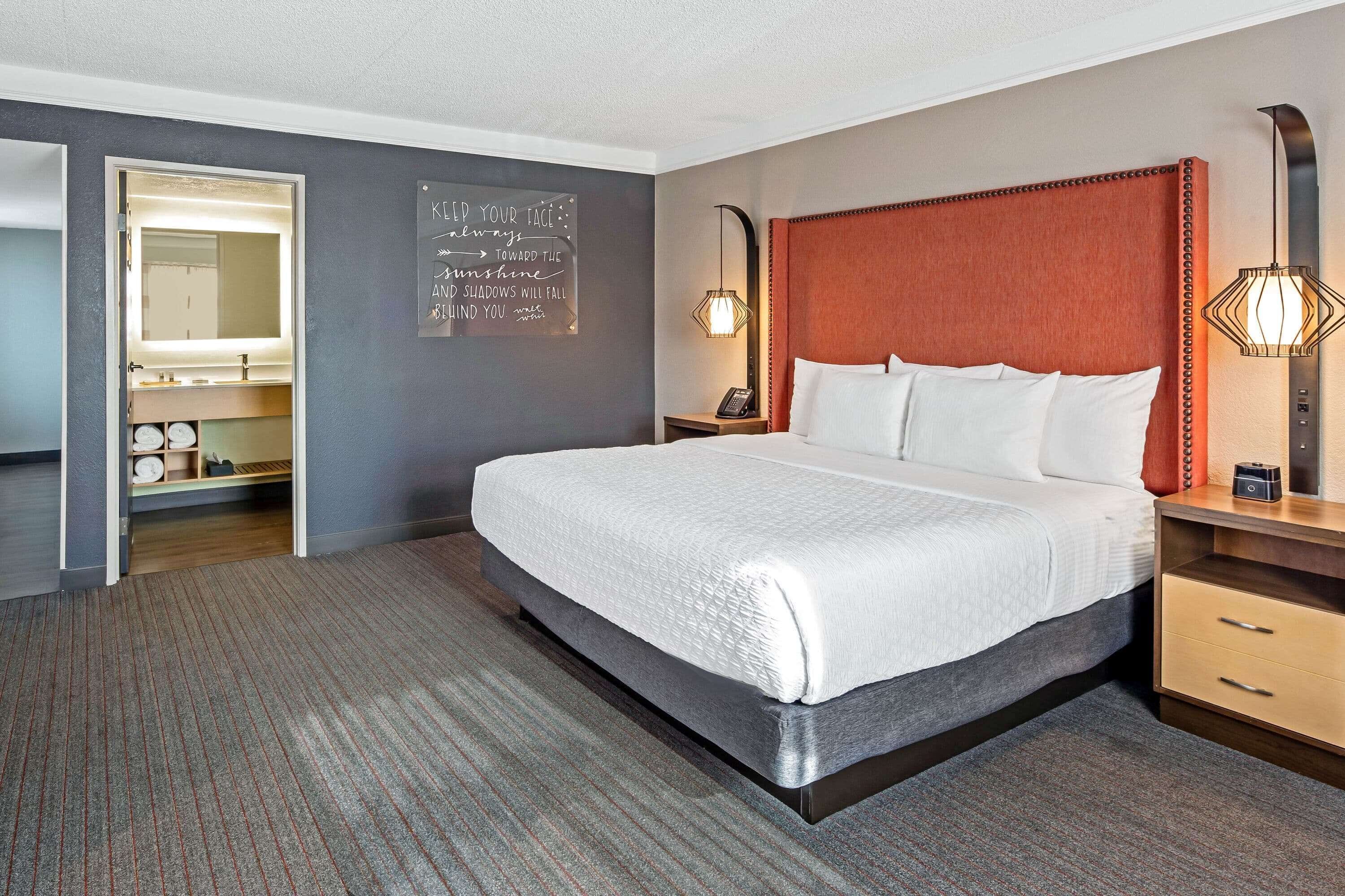 A hotel room with a large bed, a bedside table with a lamp, a nightstand, and a wall-mounted mirror.