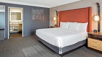 A hotel room with a large bed, a bedside table with a lamp, a nightstand, and a wall-mounted mirror.