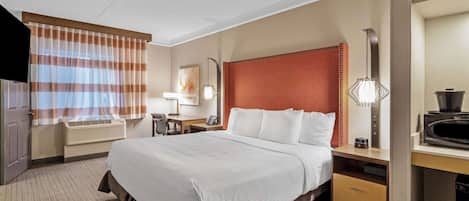 A hotel room with a large bed, a desk with a computer, a television, and a window with striped curtains.