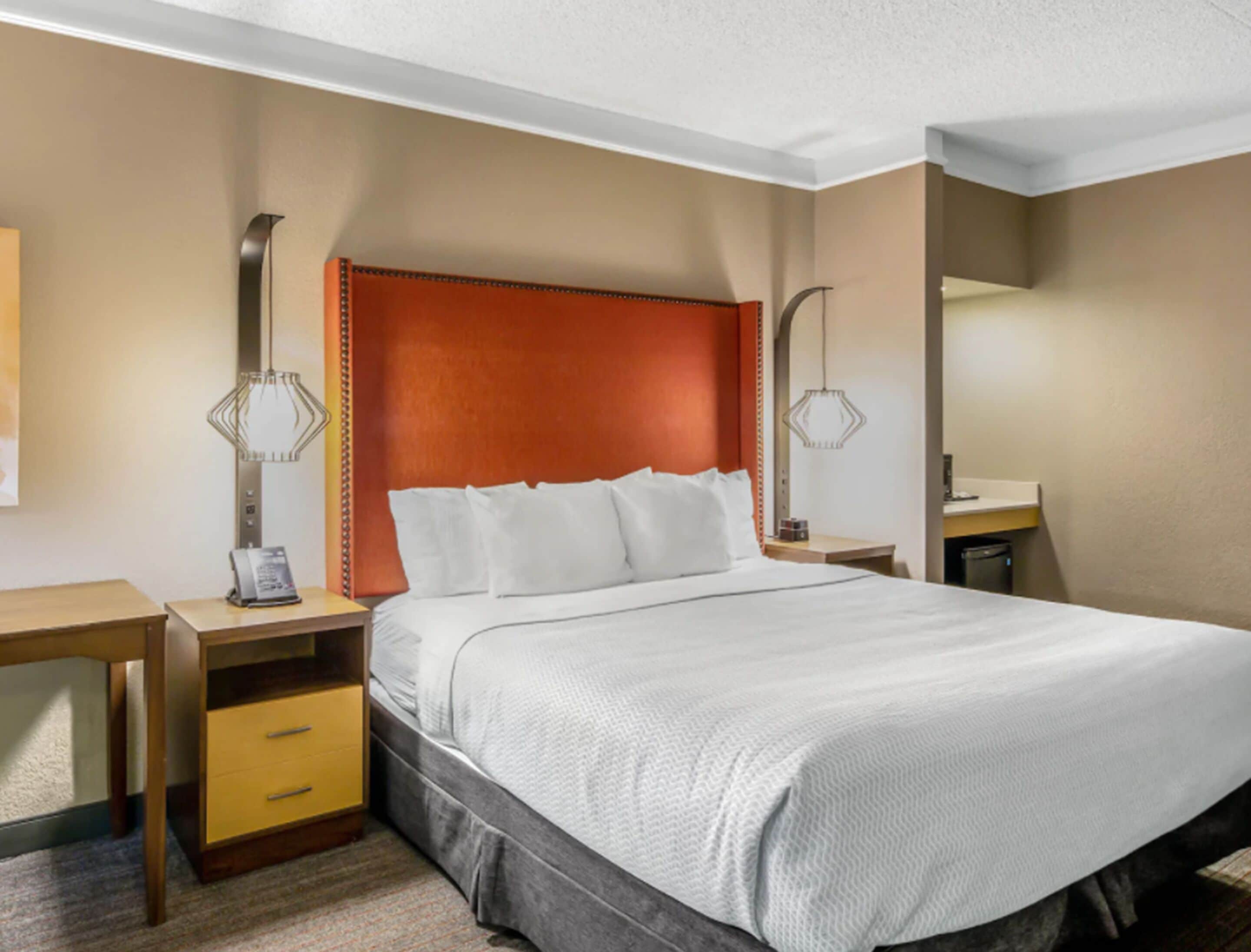A hotel room with a large bed, a wooden nightstand, a desk, and a mirror.