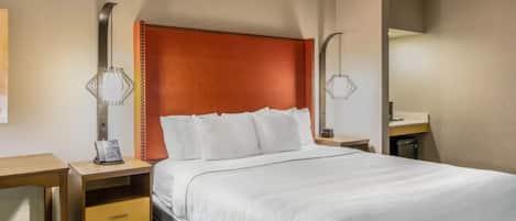 A hotel room with a large bed, a wooden nightstand, a desk, and a mirror.