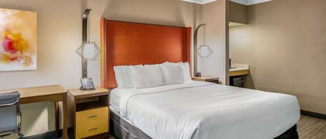 A hotel room with a large bed, a desk with a chair, a nightstand, and a wall-mounted lamp.