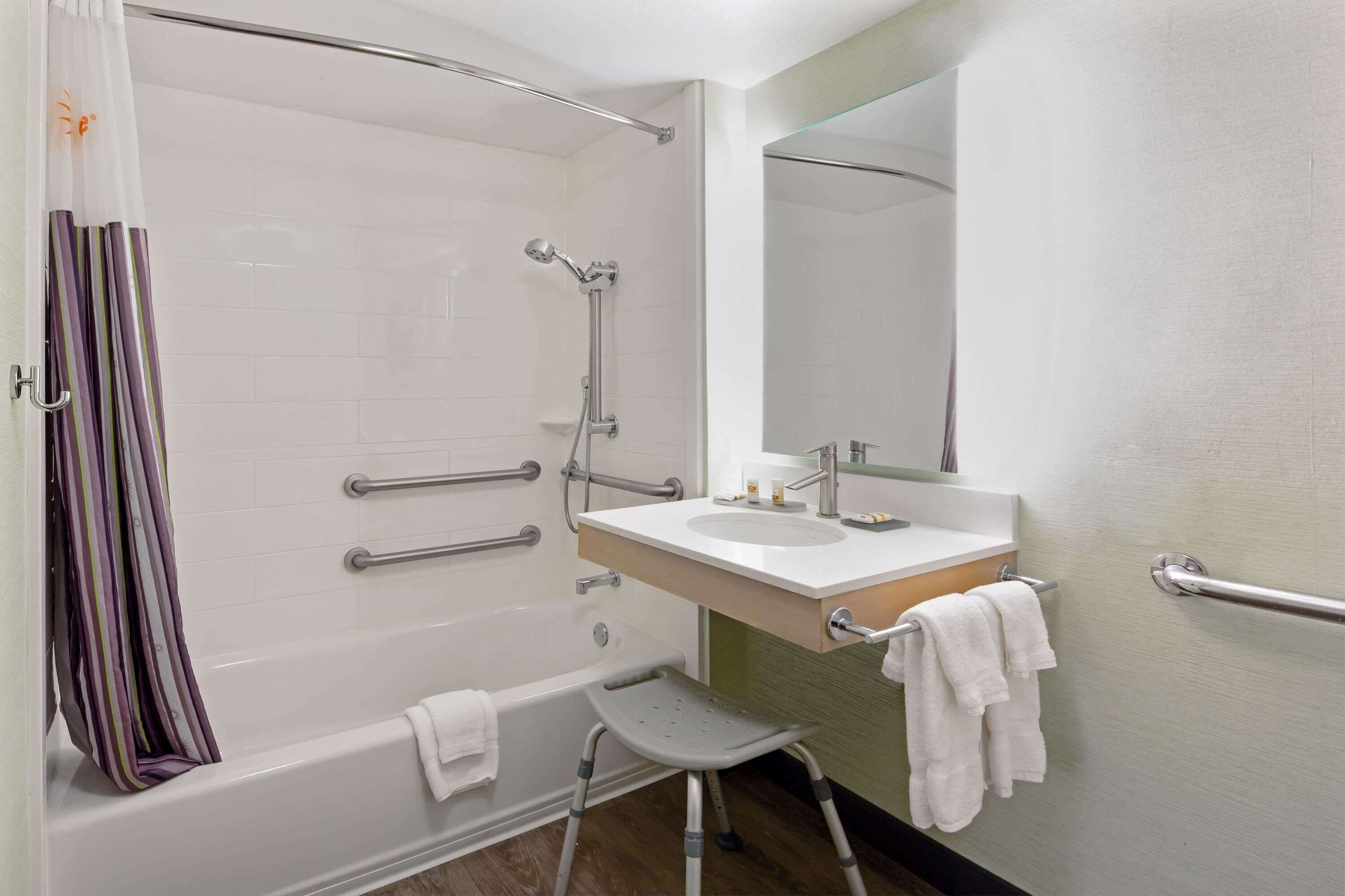 Un baño con bañera, ducha, lavabo, espejo y un taburete.