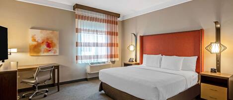 Ein Hotelzimmer mit Bett, Schreibtisch, Stuhl und einem großen Fenster mit Vorhängen.