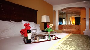A hotel room with a neatly made bed, a tray with a bottle, glasses, and a vase with flowers.
