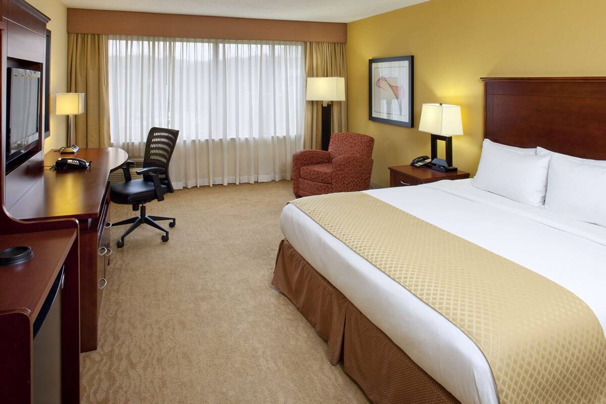 Une chambre d’hôtel avec un grand lit, un bureau avec un téléphone, une chaise et un téléviseur.