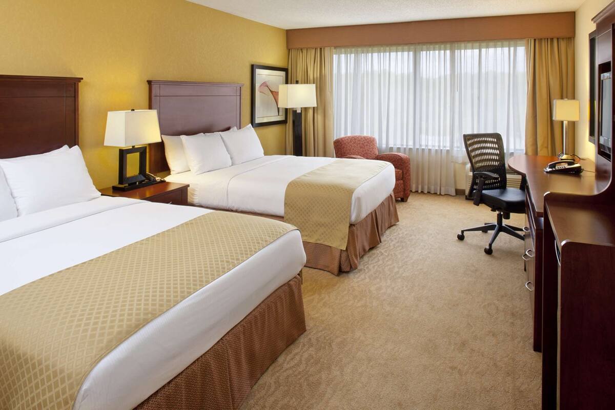 Une chambre d’hôtel avec deux lits, un bureau, une chaise et une fenêtre avec des rideaux.