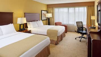 A hotel room with two beds, a desk, a chair, and a window with curtains.
