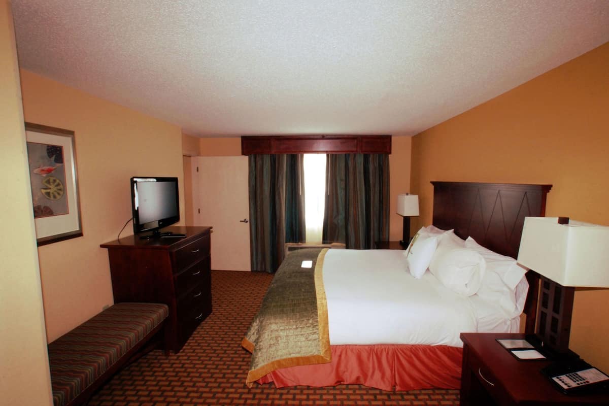A hotel room with a bed, a television, a desk, a chair, a dresser, and a window with curtains.