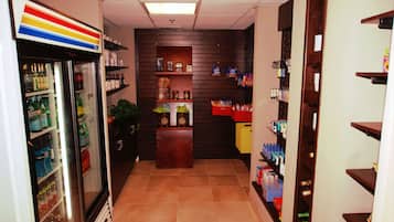 A hallway with a refrigerated display case on the left, shelves with various items in the center, and a counter with a cash register on the right.