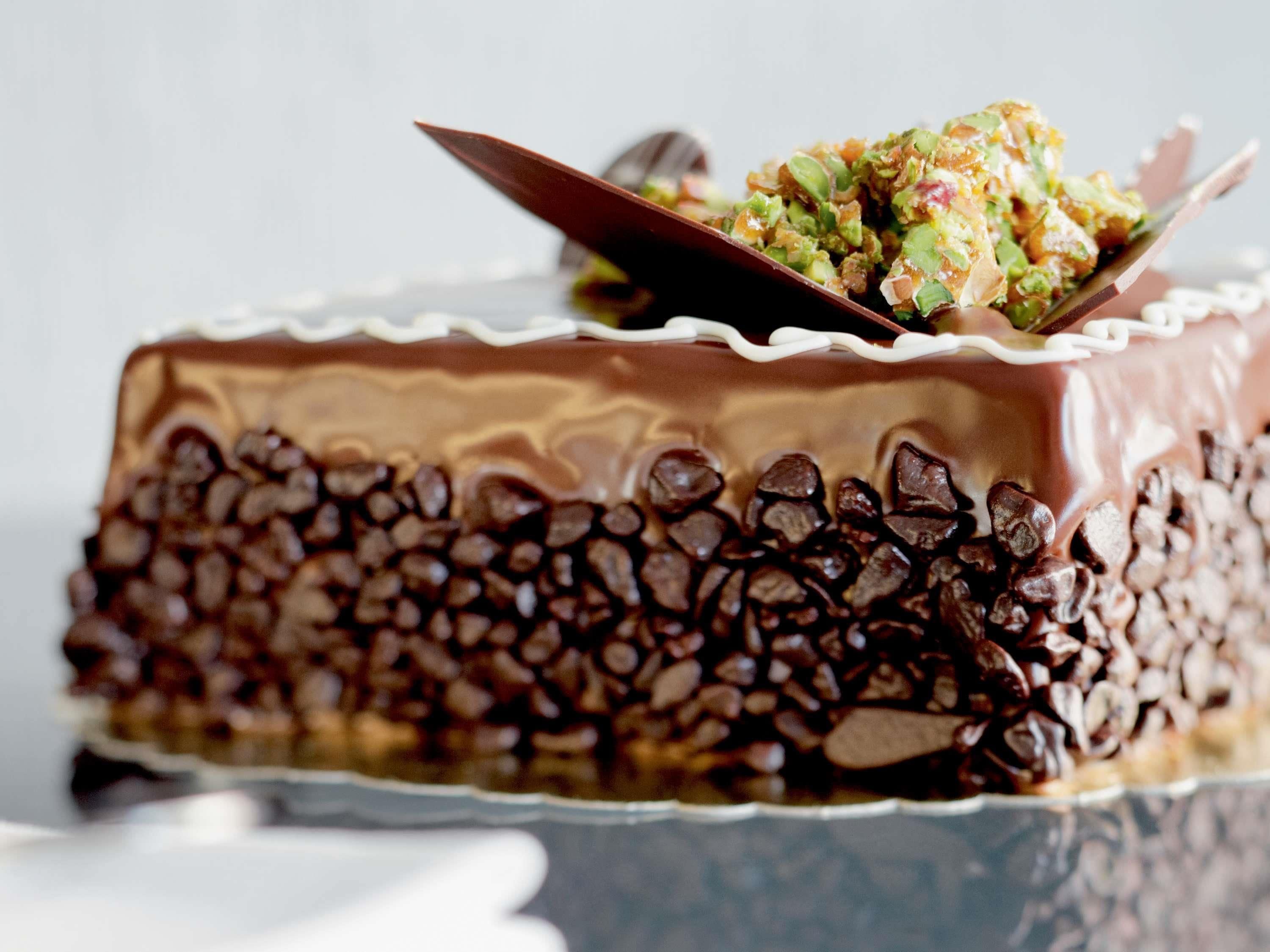 Een chocoladetaart met een glanzende chocoladelaag en een witte rand, versierd met een groene en witte garnering.