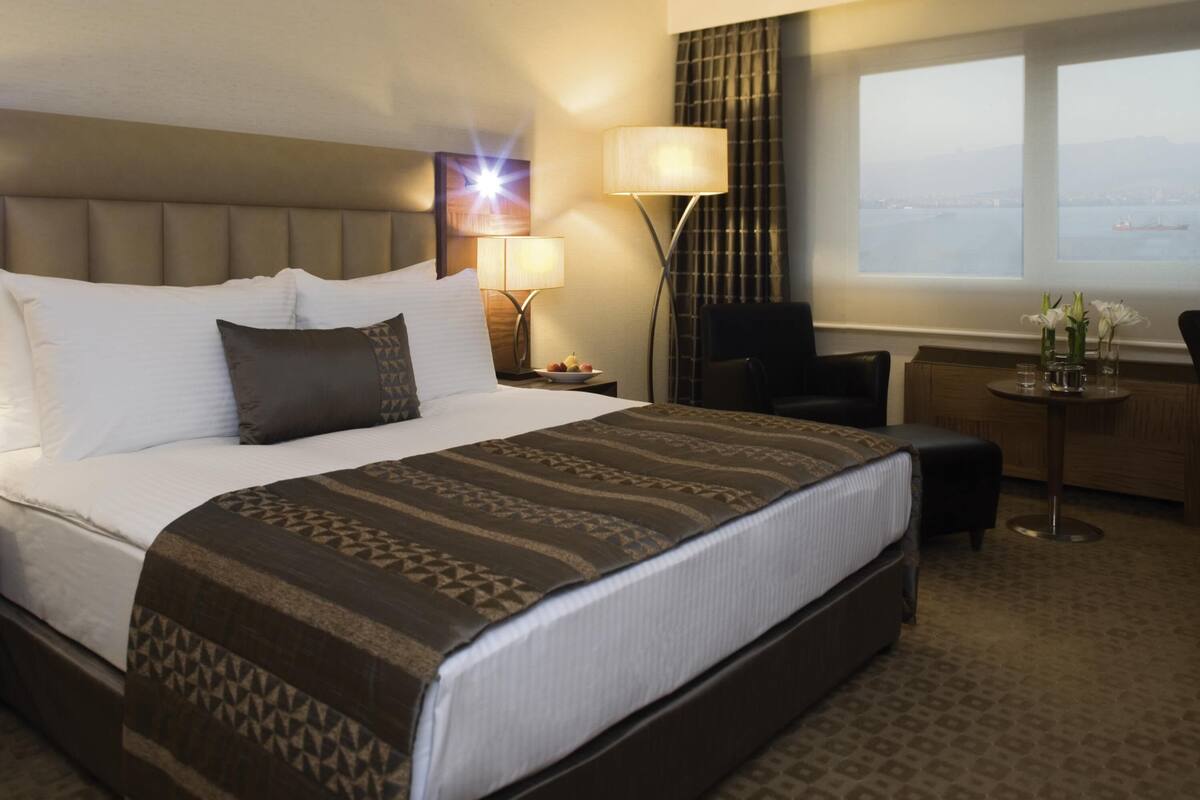 Habitación de hotel con una cama grande, un escritorio, una silla, una lámpara y vistas al mar.